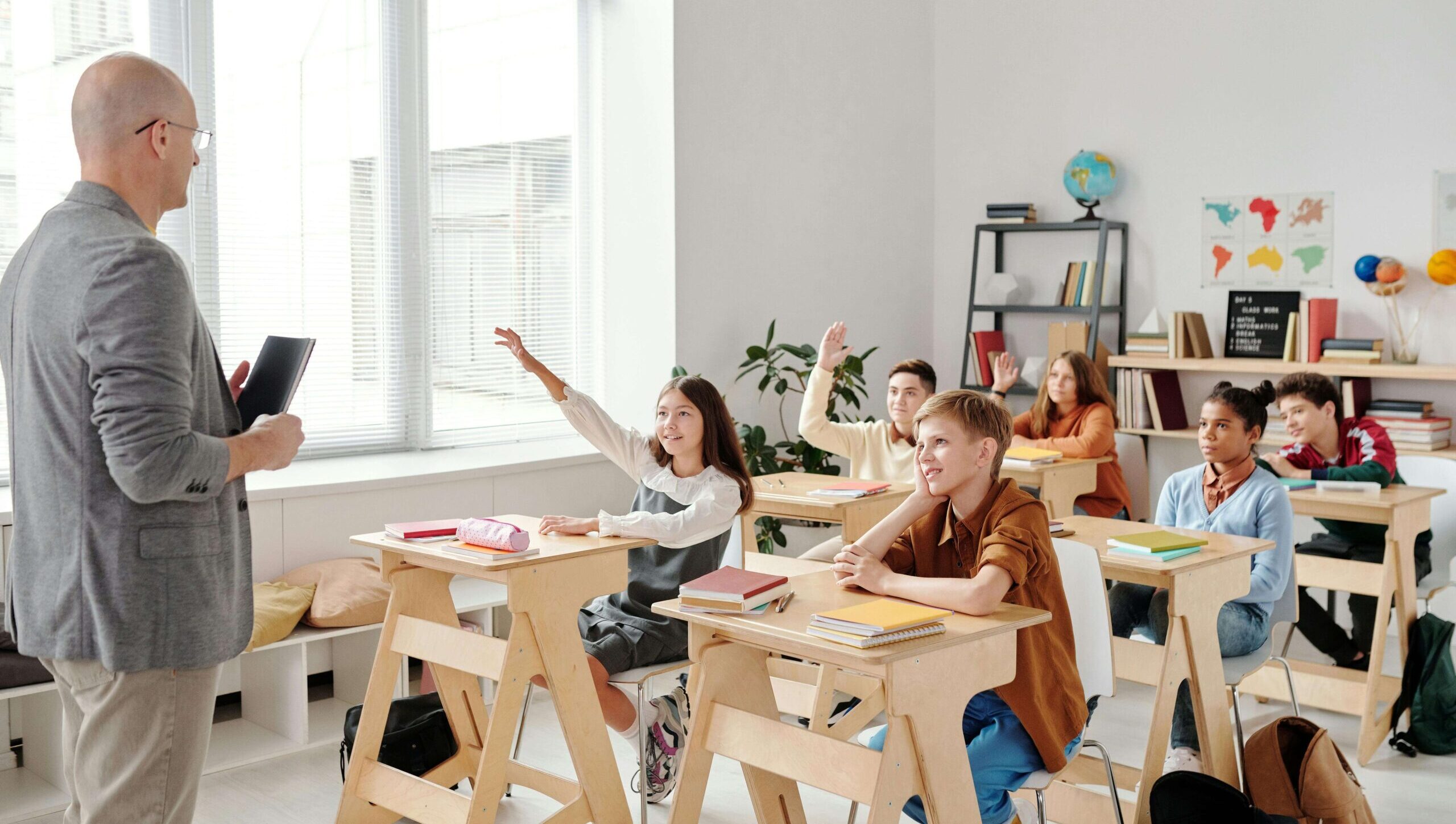 A teacher looking at his student raising their hands to a question.