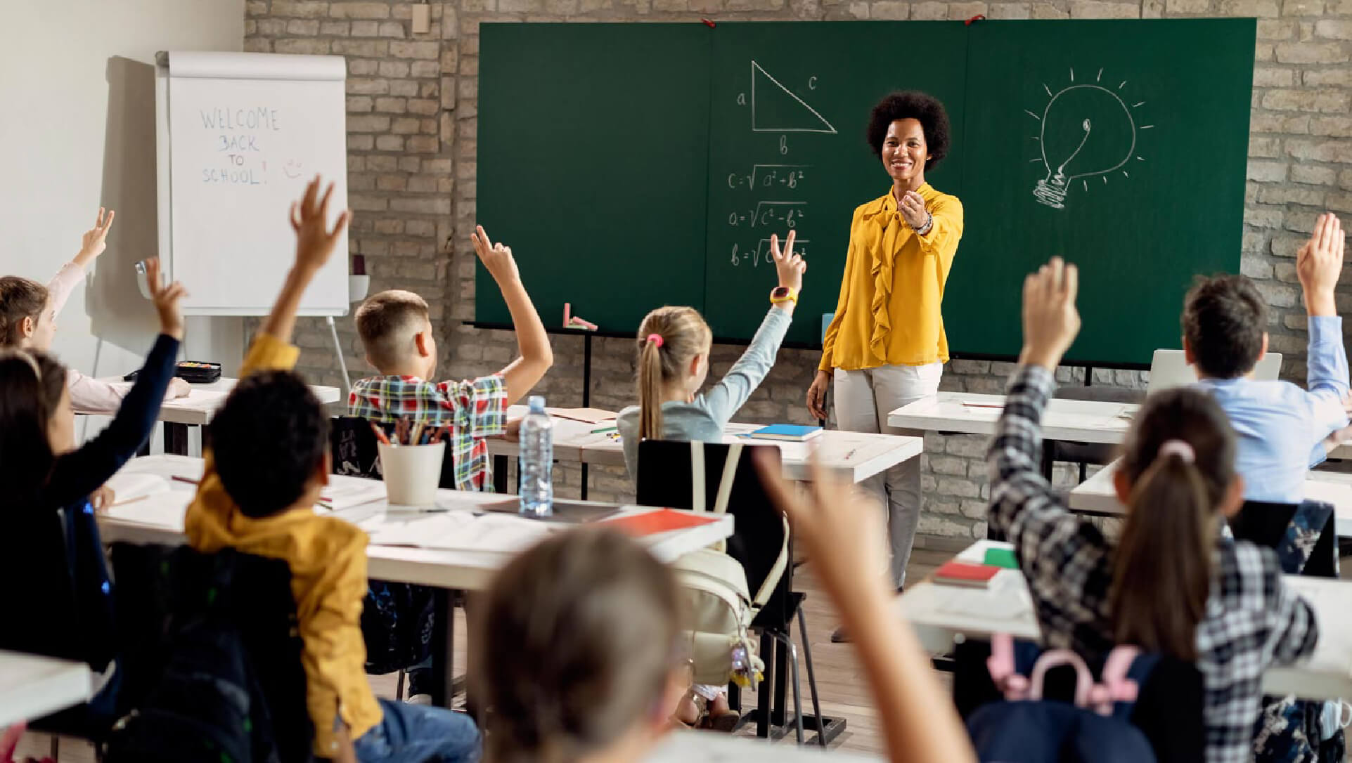 Teacher smiling and looking at her students raising their hands to answer a question.