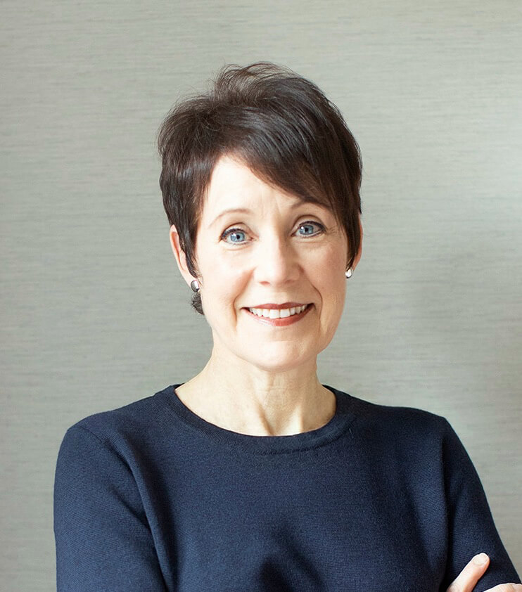 A woman with short dark hair wearing a dark navy top, smiling softly against a neutral background.